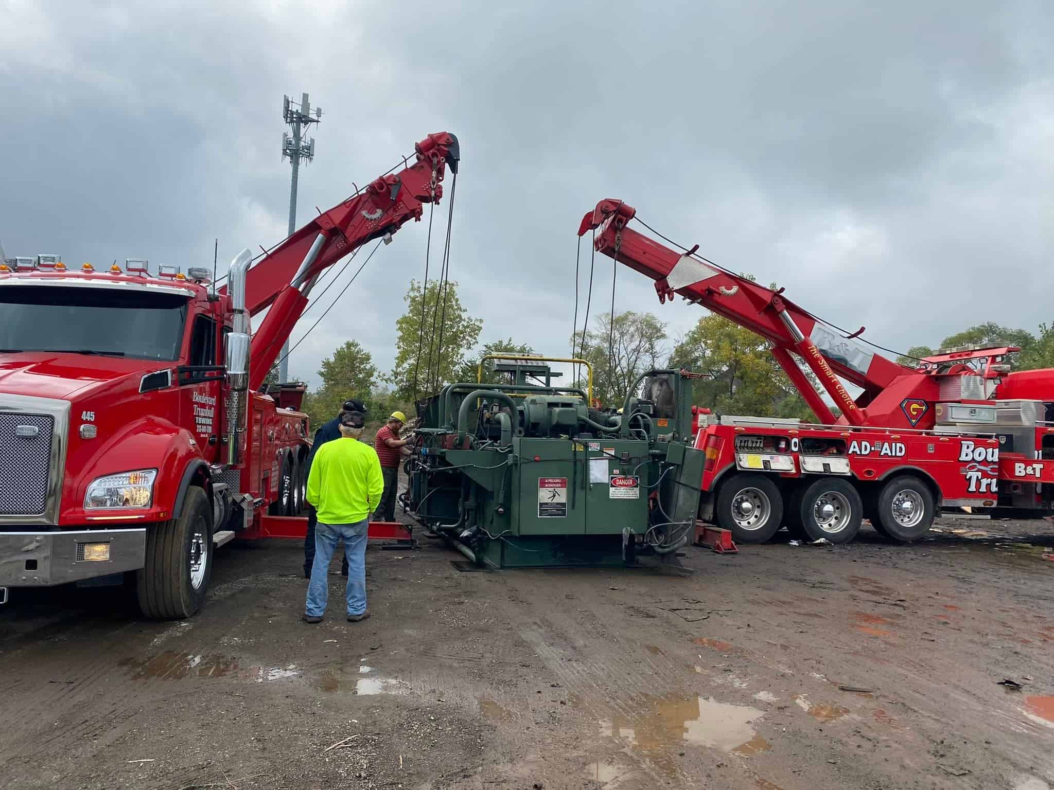 two wrecker tow trucks lifting construction equipment.