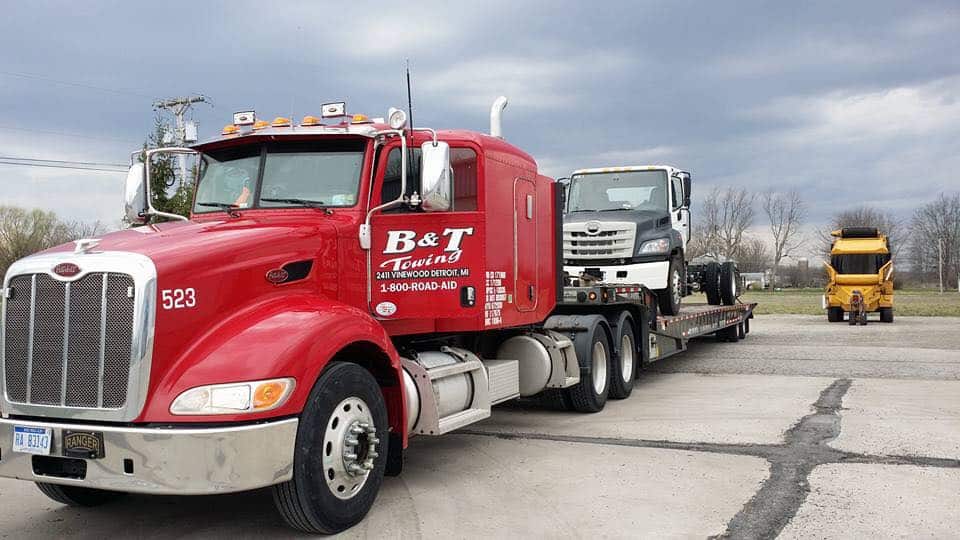 b&t towing truck flatbed with large vehicle on top.